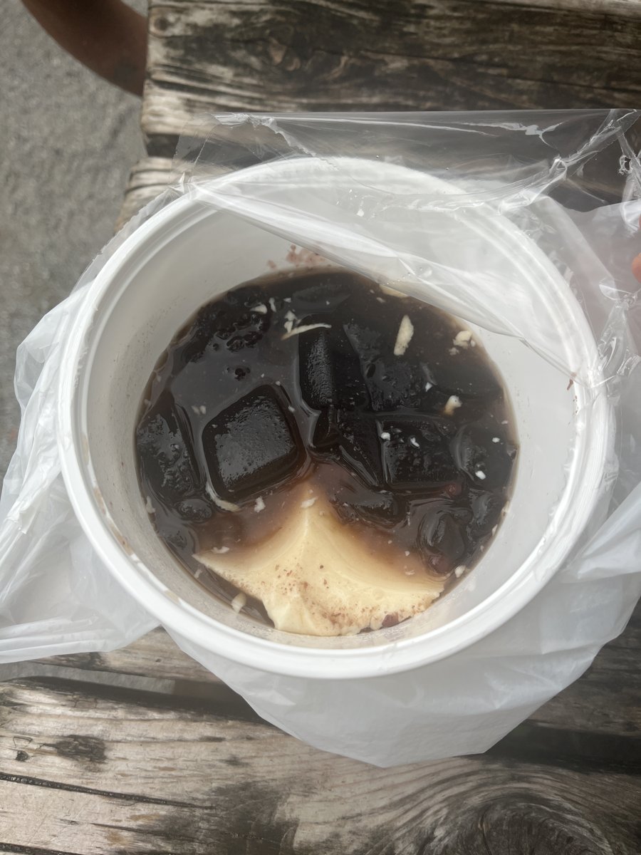 持ち帰りの豆花のカップ。白い豆花の上に黒い仙草ゼリー、黒もち米、あずき、きび砂糖シロップ