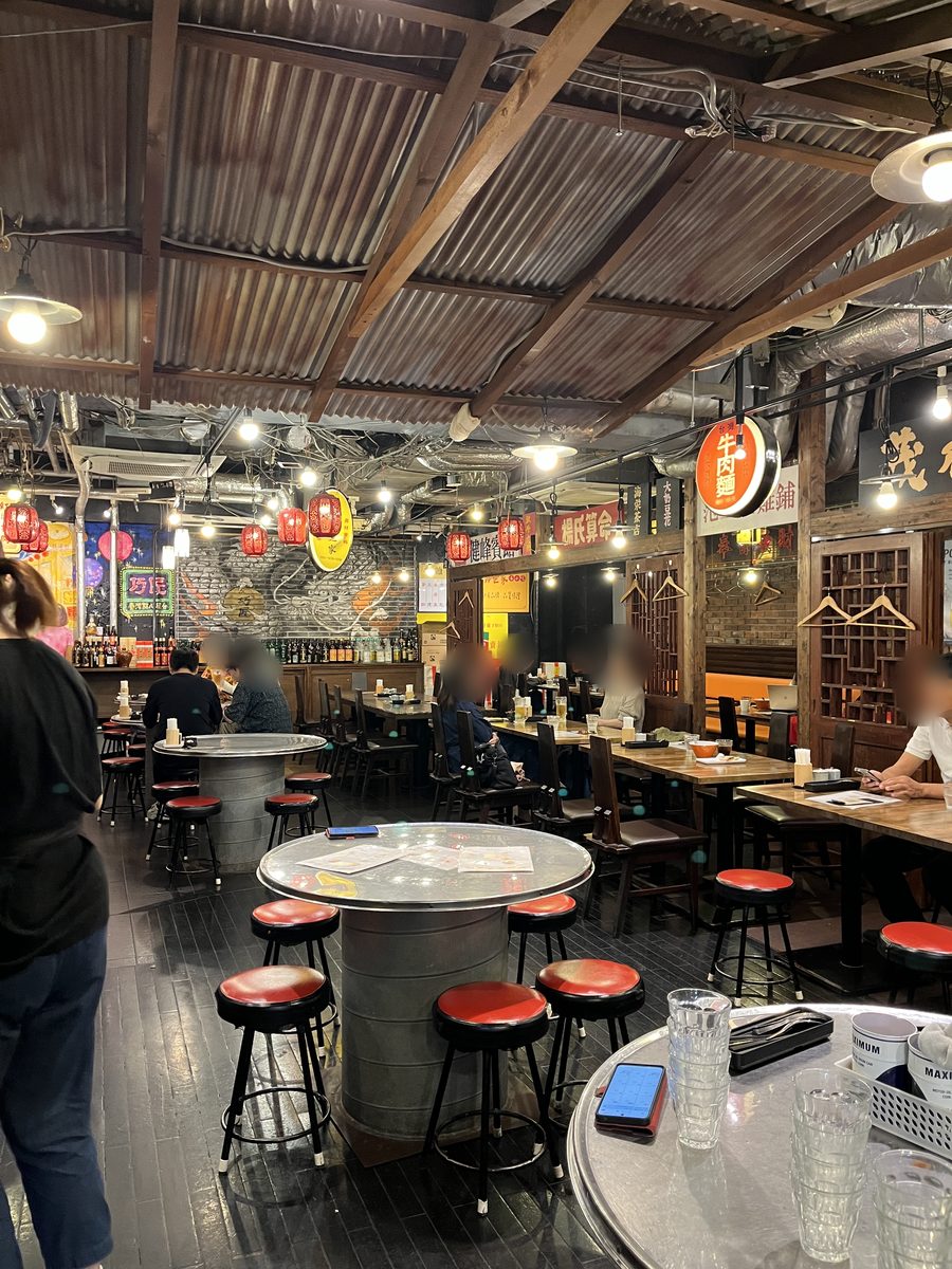 地下の広い店内。トタン屋根のような天井に赤い提灯が下がり、丸いスチールのテーブルと赤い丸椅子が並んでいる