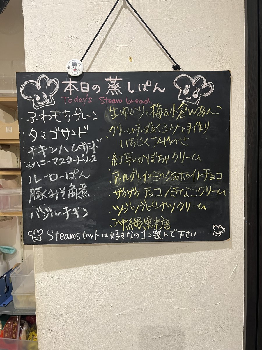 壁にかかった黒板「本日の蒸しぱん」。ふわもちプレーン、タマゴサラダ、ルーローぱん、クリームチーズ&くるみなど、この日の蒸しパンの種類が手書きで並んでいる